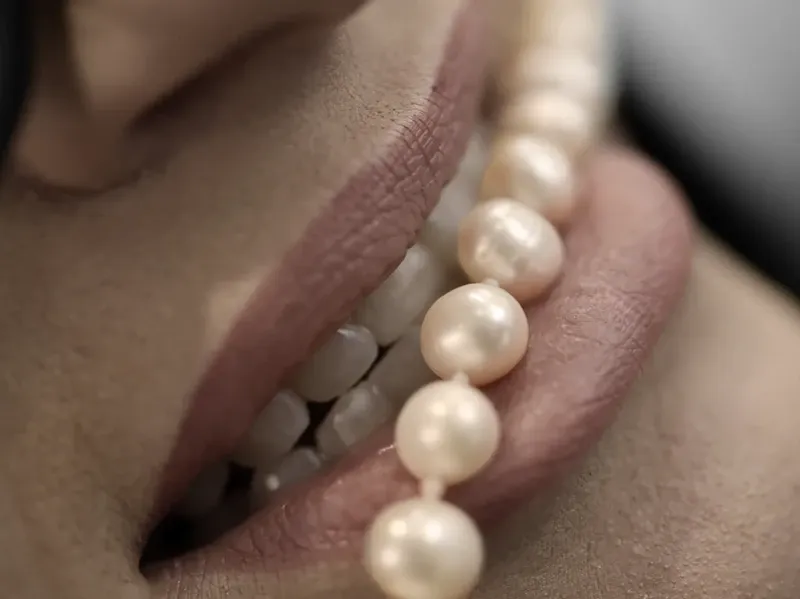 Close-up of a smile with a strand of pearls resting against the lips